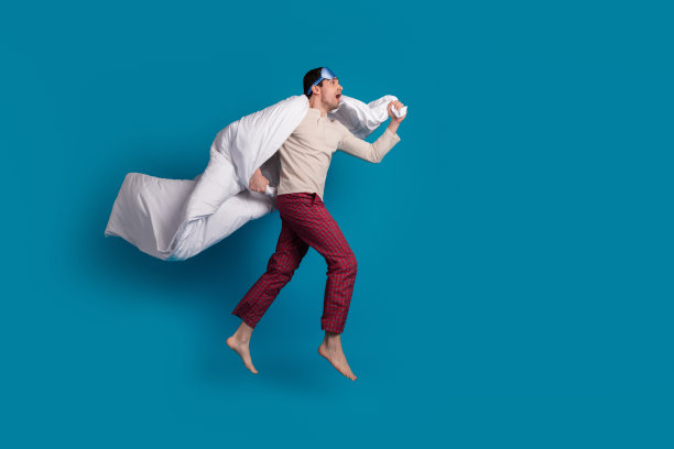 完整的照片英俊的年轻人飞行跑步毯子穿着睡衣过夜，早上好孤立的蓝色背景图片下载