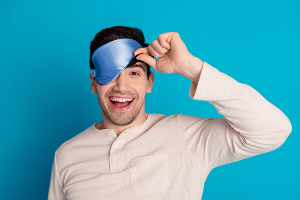 照片肖像英俊的年轻人偷看眼睛蒙着面具睡觉穿着睡衣过夜的人早上好孤立的蓝色背景图片下载