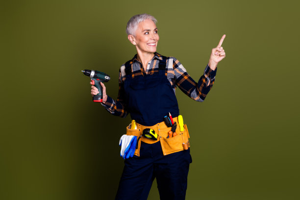 照片中成熟的女性专业机械师手持钻头，看起来空无一人，穿着蓝色工作服，孤立在卡其色背景上图片下载