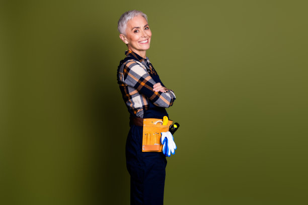 照片可爱的退休妇女手工工作工程师交叉双手侧面穿着蓝色工作服整体孤立的卡其色背景图片下载