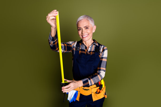 有吸引力的成熟的妇女的照片，专业的机械测量带穿着蓝色工作服的整体孤立的卡其色背景图片下载