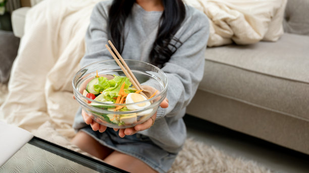 一个美女坐在客厅里拿着健康的沙拉碗的特写照片。图片下载