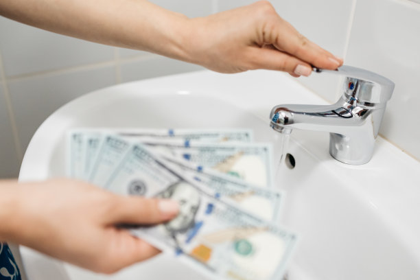 一个女人拿着钱，背景是一个有水的水槽。水电费估算、维修和管道维修服务。家庭财务支出概念。图片下载
