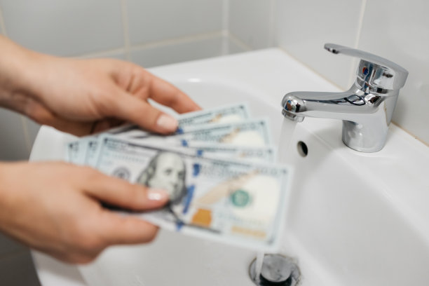 女人的手拿着钱，背景是一个水槽和一个水龙头。公用事业，支付和储蓄的概念。图片下载