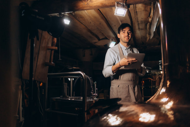 啤酒质量控制。戴着围裙和防护面具的男子拿着数码平板电脑看着啤酒厂的啤酒杯，自由的空间图片下载