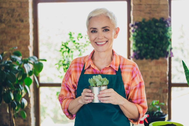 照片积极的好心情高级妇女穿着围裙护理鲜花拿着花盆在室内房屋车间图片下载