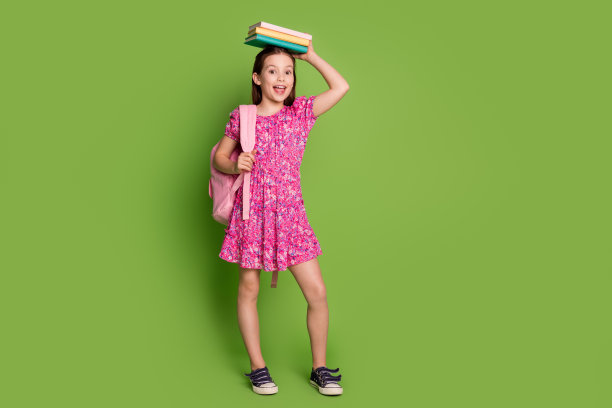 可爱的女学生的全尺寸照片，抱着书头，穿着粉红色的衣服，孤立在绿色的背景上图片下载
