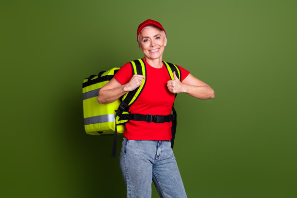 可爱的退休女士的照片，快递服务员工保暖袋拇指向上，穿着红色制服工作服，孤立在卡其色背景上图片下载