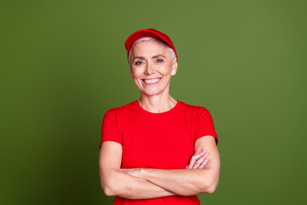 照片中，有魅力的成熟的女性专业送货员双手交叉，穿着红色制服工作服，孤立在卡其色背景上图片下载