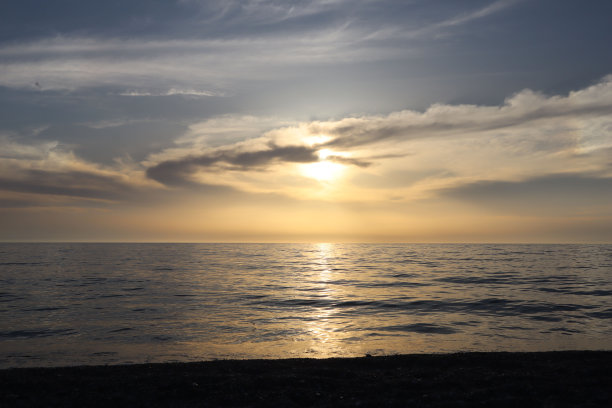 美丽的夕阳落在海面上，太阳在云的后面，照片作为背景图片下载