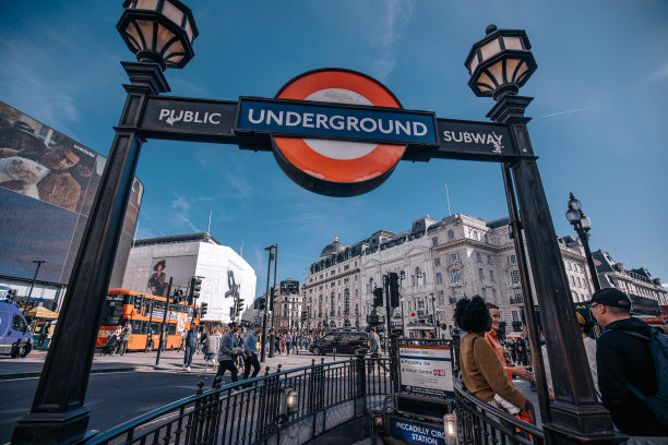 摄政街的伦敦地铁站入口，有红色的圆圈标志，路灯和蓝天。牌子上写着“公共地铁”，有行人经过，背景是一辆公共汽车。图片下载