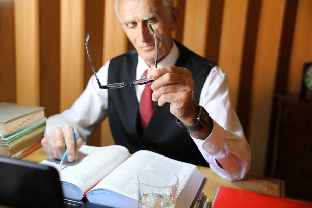 一位戴着眼镜的老人坐在办公室里阅读商业书籍图片下载