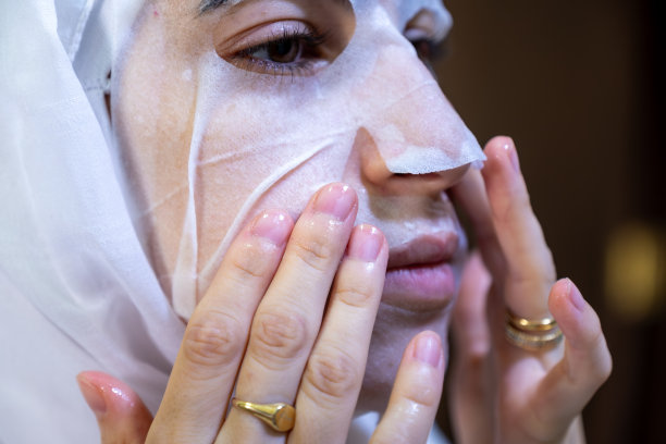 戴着头巾的阿拉伯穆斯林女性在水疗或浴室中敷面膜，看着自己的脸微笑图片下载