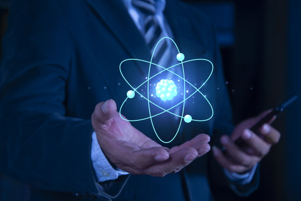 商人手持创意原子在蓝色背景。核聚变概念，无穷无尽的能源，廉价的电力，未来的技术。科学与未来理念图片下载