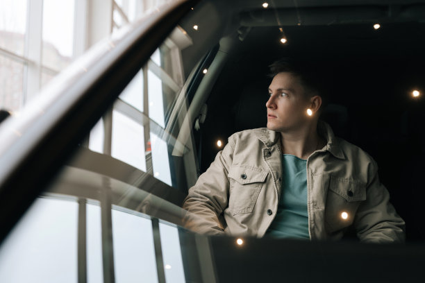 透过挡风玻璃拍摄的照片显示，自信的男性顾客坐在汽车副驾驶座位上系好安全带。年轻的买主在经销商处挑选新车。图片下载