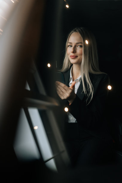 通过挡风玻璃的垂直照片，可以看到坐在汽车前座用智能手机看新闻的迷人女乘客。漂亮的年轻女子在浏览手机图片下载