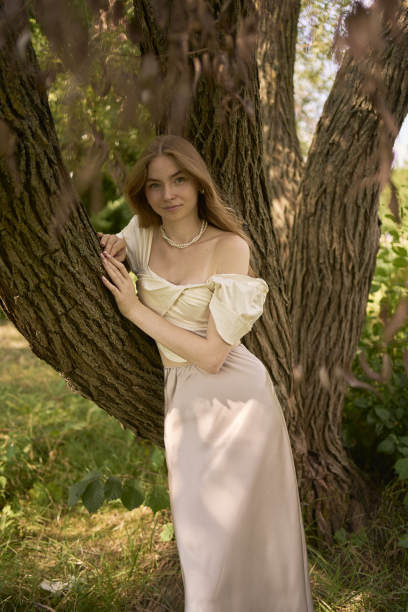 一个漂亮的十几岁的女孩，穿着丝绸裙和紧身胸衣，在公园里和河边散步图片下载