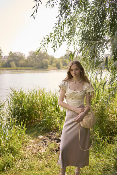 一个漂亮的十几岁的女孩，穿着丝绸裙和紧身胸衣，在公园里和河边散步图片下载