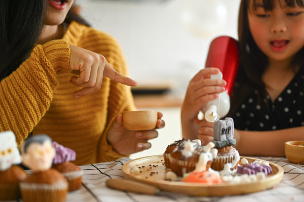 年轻漂亮的妈妈给可爱的女儿拍了一张照片，她拿着手机在厨房里装饰着诡异的纸杯蛋糕图片下载