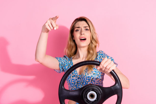 照片中，迷人的年轻女子穿着时髦的蓝色印花衣服，在粉红色的背景上开着车，惹恼了交通堵塞图片下载