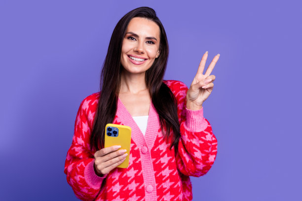 照片迷人的积极的女人穿粉红色的开襟羊毛衫显示v字聊天现代小工具孤立的紫色背景图片下载