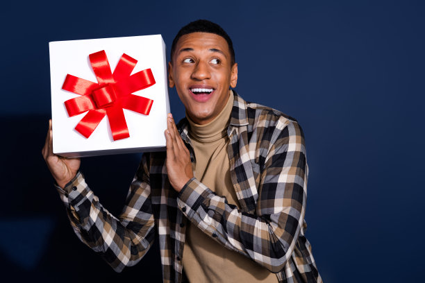 照片中兴奋的酷男穿着格子衬衫，拿着礼盒看着空旷的空间孤立的蓝色背景图片下载