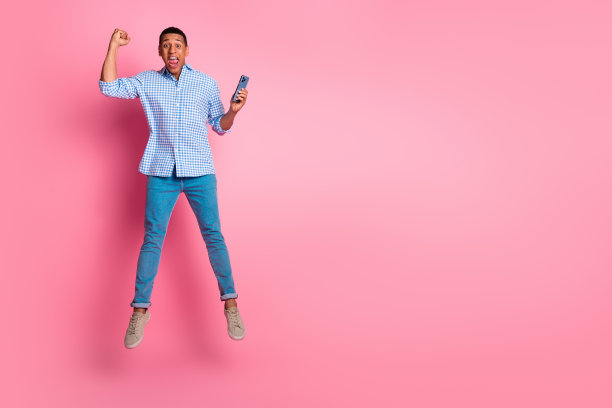 全身照片的幸运自信的家伙穿格子衬衫跳跃赢得游戏现代小工具空的空间孤立的粉红色背景图片下载