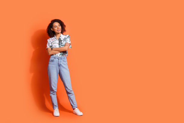 照片的年轻女士棕色波浪的头发穿着牛仔裤和夏威夷衬衫折叠臂看信息孤立的橙色背景图片下载