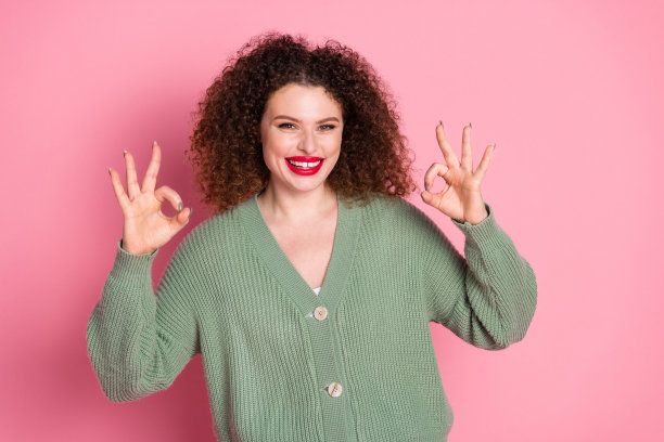 照片中，开朗可爱的漂亮女人穿着时尚的卡其色衣服，标志孤立在粉红色的背景上图片下载