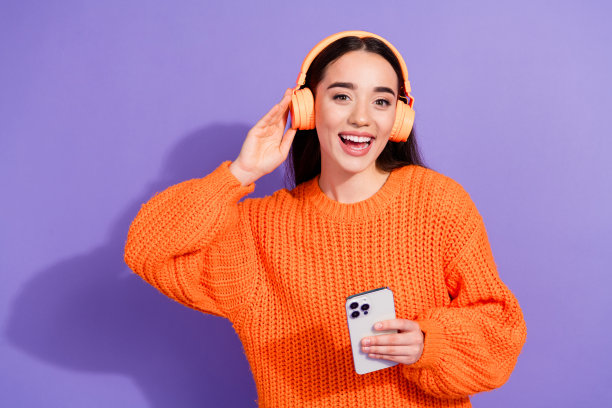 可爱开朗的漂亮女孩的照片，穿着时髦的橙色衣服，在紫罗兰色的背景上听音乐图片下载