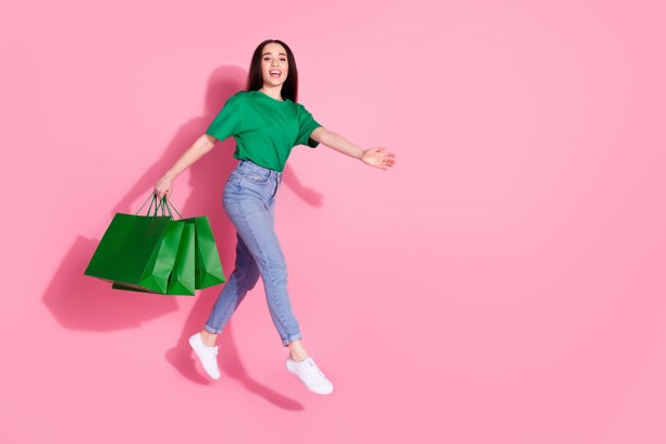 迷人积极的女人全身照片穿绿色t恤跳抱购物者空空间孤立的粉红色背景图片下载