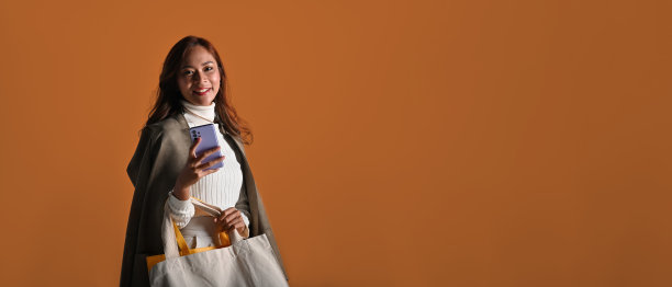 照片中，年轻的亚洲女性带着布袋和手机，看起来很聪明，拍摄于摄影棚背景，黑色星期五购物的概念。图片下载