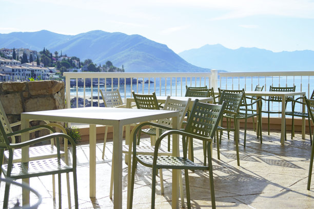 咖啡馆露台上空荡荡的桌椅，映衬着城市、大海和山脉图片下载