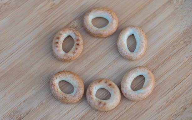 6个百吉饼以椭圆形排列在浅色木质表面上，以高角度拍摄产品照片图片下载
