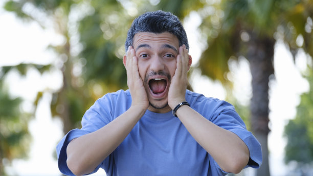 一个黑头发的男人双手捂着脸，在树林里带着惊讶的表情看着镜头图片下载
