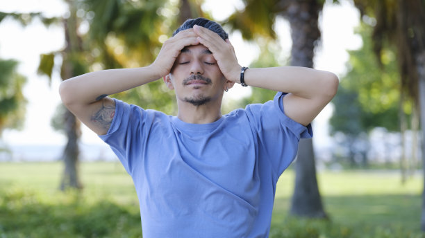 一个黑头发的男人站在树林里，双手抱头，露出痛苦的表情图片下载