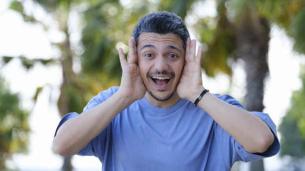 一个黑头发的男人双手捂着脸，在树林里带着惊讶的表情看着镜头图片下载