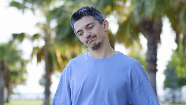 一个黑发男子站在树林里，带着悲伤的表情看着镜头图片下载