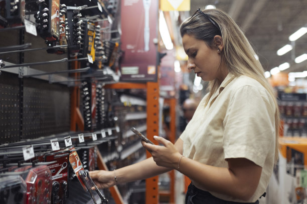 在商店里买工具的女人的侧视图。她会在手机上查看工具的图片，以确保自己不会买错东西图片下载
