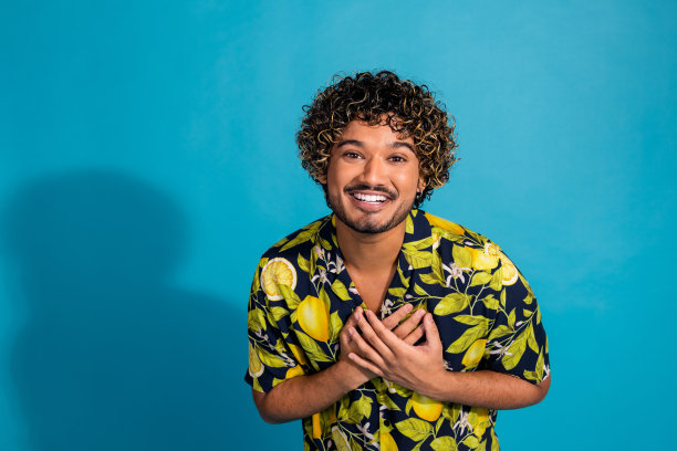 照片欣赏感激的男人波浪发型，穿着印花衬衫，手掌放在胸前孤立的蓝色背景图片下载