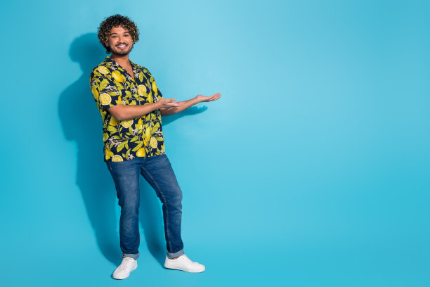全长照片满意的男人穿着印花衬衫牛仔裤手臂呈现产品空白空间孤立的蓝色背景图片下载