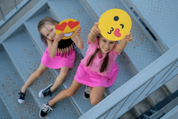 穿着粉色裙子的搞笑女孩坐在楼梯上，展示着心形和亲吻的表情符号图片下载