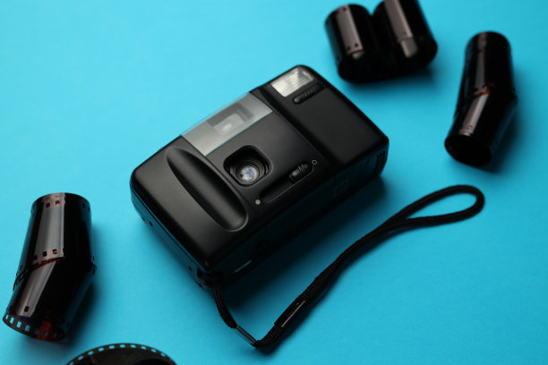 一台黑色的相机放在蓝色的表面上，上面放着一堆胶卷。相机被胶卷包围着，胶卷大小不同，颜色也不同图片下载