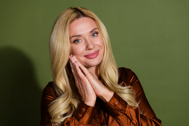 照片的漂亮可爱的女人穿着丝绸时尚的衣服两个手臂脸颊孤立的卡其色背景图片下载