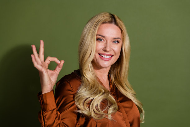 照片迷人可爱的女人穿着缎面时尚的衣服手臂ok标志孤立的卡其色背景图片下载