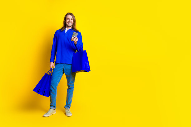 有趣的照片，好积极的男人穿着时髦的蓝色衣服，拿着包裹，在黄色背景上孤立的空白空间图片下载