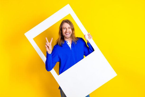 照片中开朗积极的酷男人穿着时髦的衣服，手拿纸框v字孤立在黄色背景图片下载