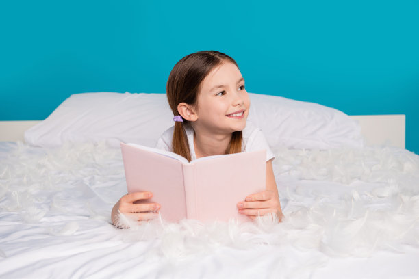 漂亮的梦幻可爱的女孩躺在舒适的床上的照片，在蓝色的背景空的空间隔离图片下载