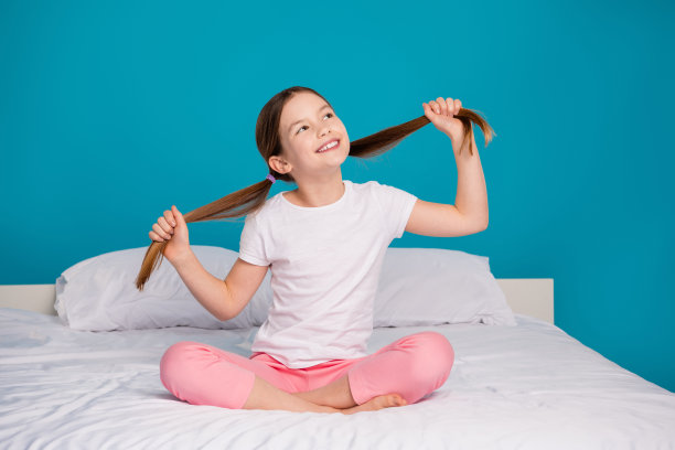 可爱小女孩的全身照片拉尾巴看空空间坐在床上睡觉的时候穿着睡衣孤立的蓝色背景图片下载