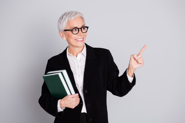 退休妇女的照片大学教授拿着书点看空穿着正装眼镜孤立在灰色背景图片下载